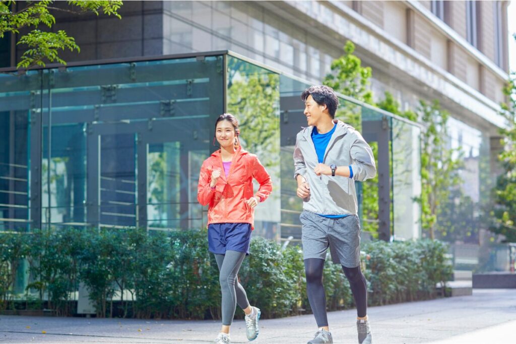 街中を仲良くジョギングする男女。明るい日差しの中で笑顔を交わしながら軽快に走っている様子