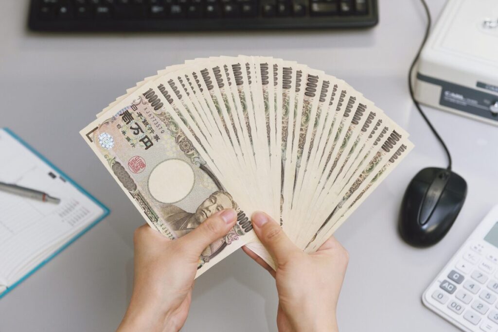 机の上で1万円札の束を両手で扇状に広げて持っている様子。年収や手取り金額、収入イメージを表す写真