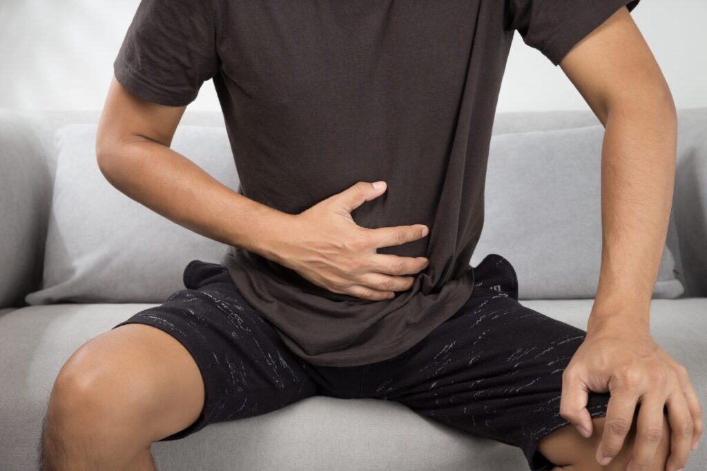 食べすぎでお腹を押さえて苦しそうにしている男性の写真